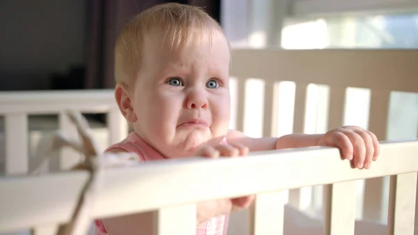 Sad baby crying in cot at home. Unhappy toddler standing in crib — Stock Photo, Image