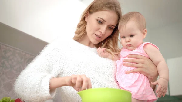 Young mother cooking with baby on hands. Baby nutrition cooking