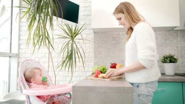 Anne mutfakta bebek için yemek yapıyor. Bebekken kızıyla yemek pişiren kadın.