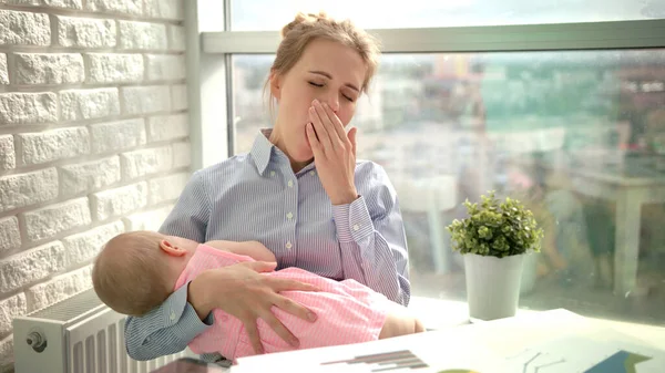 Tired woman yawn with sleeping child on hands. Sleepy mom with kid at workplace