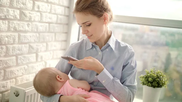 Gyönyörű nő ingben, aki mobilképet készít a lányról. Anya fotózza a babát. — Stock Fotó
