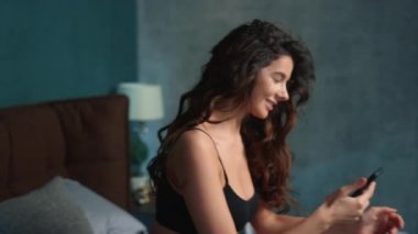 Yatakta internet telefonunda sörf yapan seksi kadın. Akıllı telefonlu seksi kız dinleniyor.