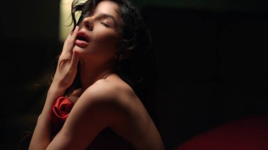 Yatakta dudaklarını ısıran tutkulu bir kadın. Çıplak kız karanlık yatak odasında saç oynuyor..