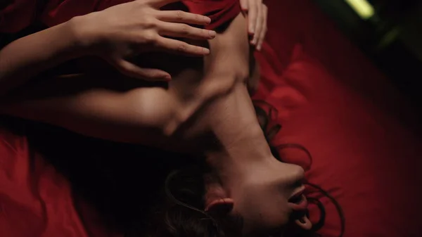 Närbild naken kvinna poserar i sängen. Sexig tjej som leker sig själv på rött sidenlakan. — Stockfoto