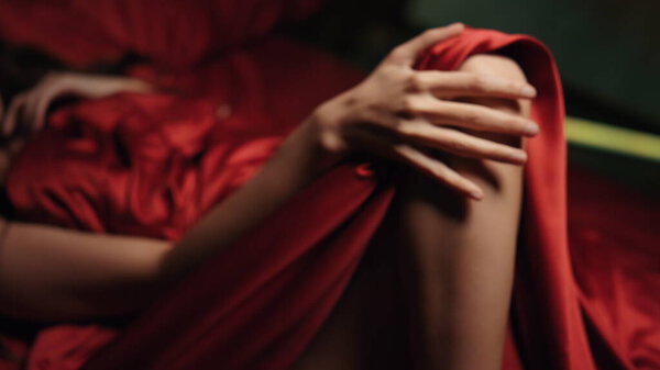 Unknown lady stroking leg in bed. Naked woman resting in red silk bed.