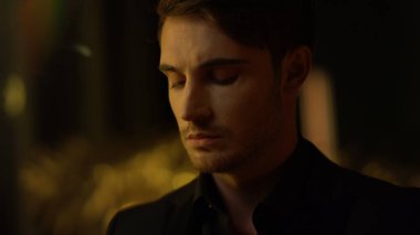 Yakışıklı üst düzey yönetici kapalı alanda kameraya bakıyor. Karanlık odada düşünceli bir adam.