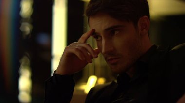 Kameraya içeride poz veren odaklanmış bir adam. Karanlık arka planda oturan düşünceli bir adam.