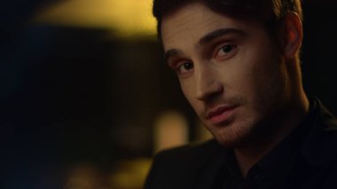 Koyu arkaplanda kaşlarını kaldıran yakışıklı bir adam. Yakışıklı adam içeride gülümsüyor..