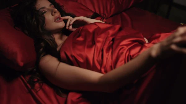 Mulher nua fechando os olhos na cama. Quente senhora acariciando corpo através de folha de seda vermelha. — Fotografia de Stock