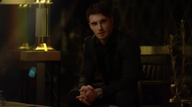 İş adamı karanlık bir iç mekanda koltukta oturuyor. Rahatlamış adam içeri bakıyor.