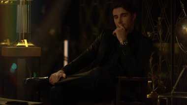 Karanlık odada bacak bacak üstüne atmış zengin bir adam. Tarz sahibi adam bir şeyler düşünüyor.