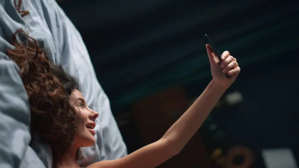 Flirty woman taking selfie mobile phone in bedroom. Smiling girl holding phone. — Stock Photo, Image