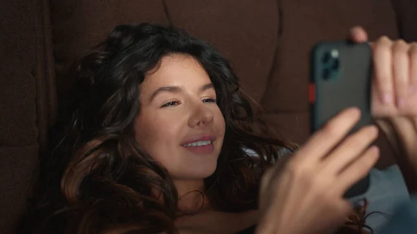 笑顔の女性は携帯電話でベッドに横たわっていた。幸せな女性は携帯電話の画面を見て — ストック写真