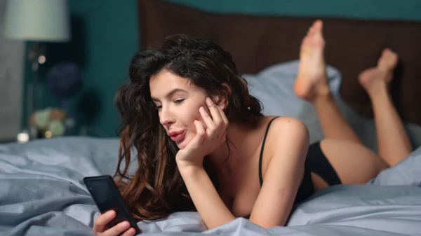 スマートフォンのベッドを使って興奮した女の子。電話でメッセージを受け取った驚くべき女性. — ストック写真