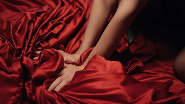 Vrouwenhanden met rood satijnen laken op bed. Onbekend meisje heeft moment plezier. — Stockfoto