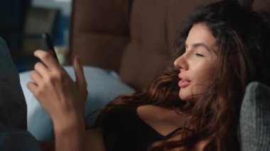Süslü bir kadın cep telefonunu yatağa koyuyor. Harika, evde boş zamanın tadını çıkarıyor.