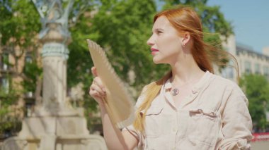 Kapalı kapılar ardında kendini sıcak hisseden bir kız. Üzgün kadın yelpaze sallıyor.