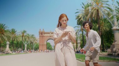 Anıtın yanındaki cep telefonuna odaklanmış bir kız. Gülümseyen adam kadınların gözlerini kapatıyor.