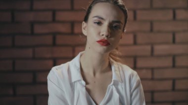 Kırmızı dudaklı, kibirli bir kadın, kendinden emin bir şekilde, tuğla telif boşluğunda kameraya bakıyor.