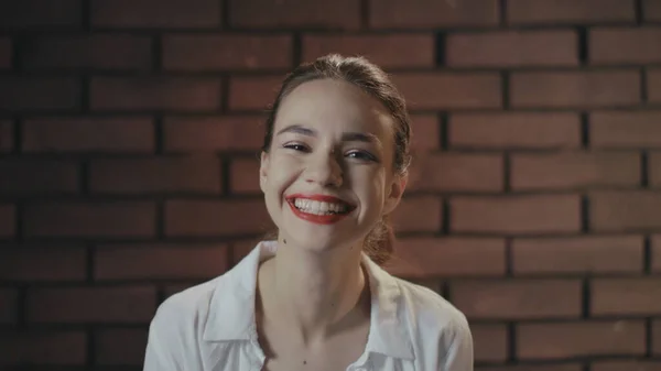 Mujer alegre riendo y posando a cámara en estudio con pared de ladrillo —  Fotos de Stock