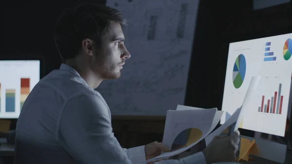 Thinking businessman looking financial charts and graphs in dark office