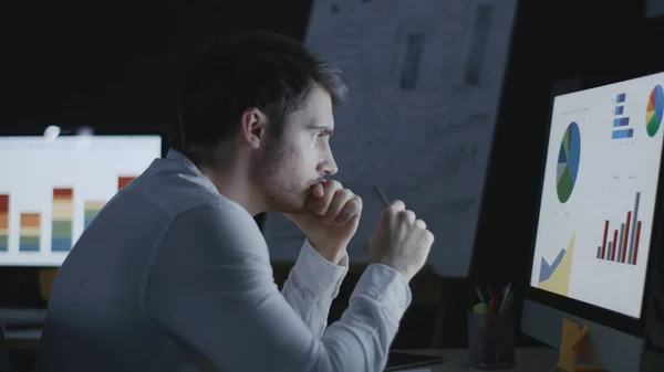 Thoughtful business analyst researching graphs and charts in night office