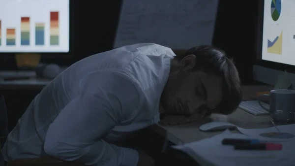 Tired business man sleeping on desk front computer screen in night office.