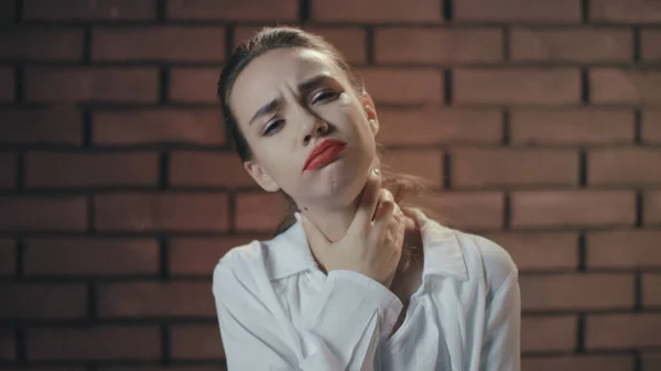 Unhappy woman feeling sore throat and coughing on brick wall background