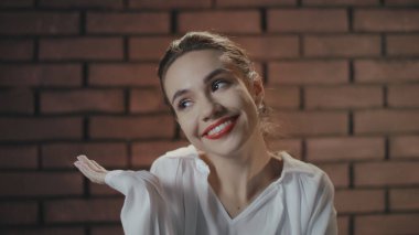 Genç kadın gülümsüyor ve utangaç bir şekilde omuzlarını silkiyor.