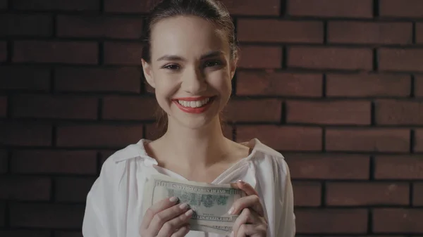 Cheerful business woman counting money for profitable investments on brick wall