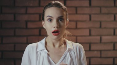 Tuğla duvardaki şoktan ağzı açık, korkmuş kadın portresi.