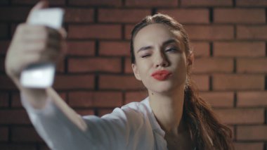 Tuğla duvardaki fotografta cep telefonu kullanan seksi kadın.