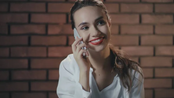 Hermosa mujer hablando teléfono inteligente y sonriendo en el fondo de la pared de ladrillo —  Fotos de Stock