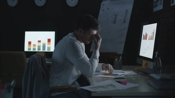 Tired businessman touching head while anayzing data and financial charts