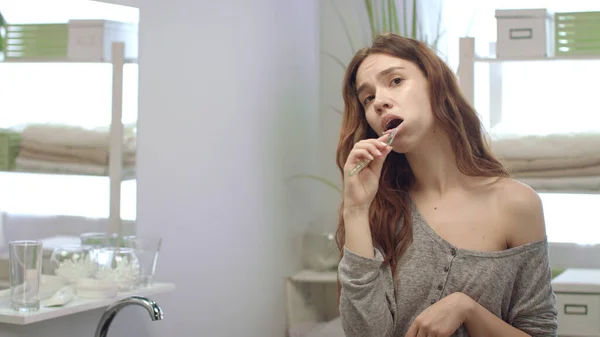 Young woman cleaning teeth with brush and posing front mirror in bath room — Stock Photo, Image