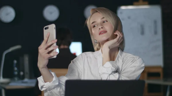 Attractive business woman making selfie on mobile phone in dark office