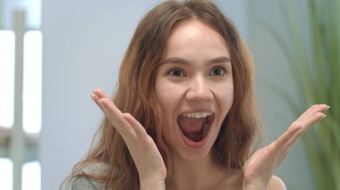 Neşeli kadın dilini gösterir, elleriyle yüzünü saklar ve yüzünü aynaya çevirir.