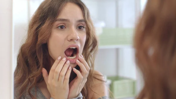 Nuori nainen, jolla on avattu suu tarkistaa hampaat peilistä kotona kylpyhuone huone kuvapankkikuva