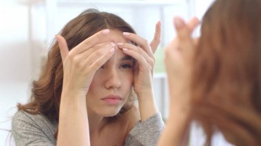 Genç kız banyo odasında cilt aynasına sivilce sıkıyor.