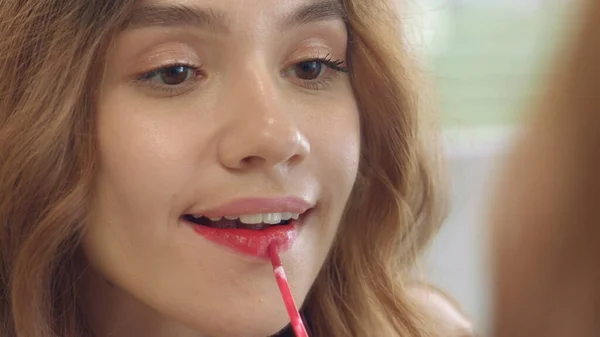 Молодая женщина, использующая жидкую помаду для макияжа губы перед зеркалом ванной — стоковое фото
