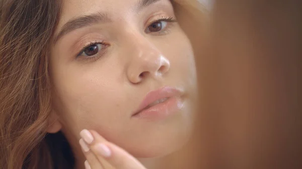 Улыбающаяся женщина наносит увлажняющий крем на кожу лица зеркало ванной комнаты — стоковое фото