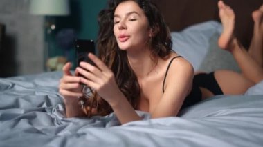 Neşeli kadın telefon yatağını gevşetiyor. Çekici bir kız. Video çağrısı, akıllı telefon.
