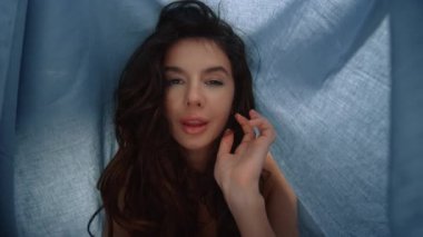 Çarşaf altında poz veren seksi bir kadın. Kamera tekstil arka planına bakan güzel kız
