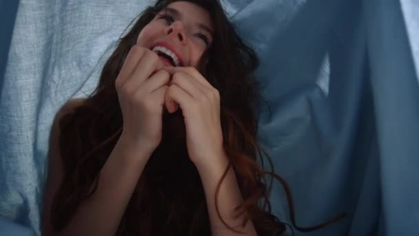아름다운 여성이 천을 두르고 있습니다. 침대 밑에서 얼굴을 만들고 있는 웃는 소녀 — 비디오
