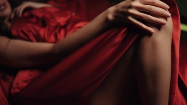 Neznámá dáma hladí nohu v posteli. Nahá žena odpočívající v červené hedvábné posteli. — Stock video