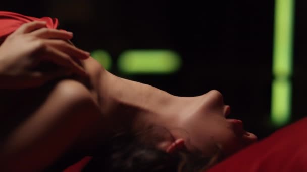 Sexig kvinna som böjer sig på sängen under rött sidenlakan. Charmig flicka ser kamera. — Stockvideo