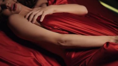Yatakta kırmızı ipek çarşaf oynayan seksi kadın elleri. Çıplak kız yatak odasında dinleniyor..