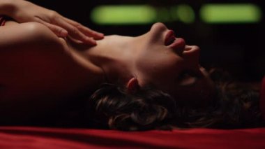 Yatakta dudaklarına dokunan baştan çıkarıcı bir kız. Ateşli bir kadın ipek çarşaflarda kendine sarılıyor.