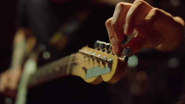 Guitarrista girando botões em fretboard no estúdio. Homem segurando guitarra no corredor. — Fotografia de Stock