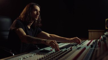 Müzik stüdyosunda çalışan düşünceli bir adam. Düzenleyici sürgüleri içeri taşıyor.